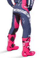 Alpinestars 2025 Techstar Dreem bukser, motocross-bukser, grå og lyserød multifarvet, set bagfra med stort hvidt Alpinestars-logo over bagen, båret med matchende panglyserøde Tech 10-støvler, slidstærkt off-road racingudstyr med forstærkede paneler