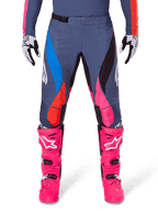 Alpinestars 2025 Techstar Dreem bukser, motocrossbukser, grå multifarvet med blå, lyserøde og orange detaljer, båret med stærkt lyserøde støvler og hvide og sorte handsker, med laserskårne perforeringer på lårene og et magnetisk taljespænde, atletisk race-fit udstyr til terrænkonkurrence