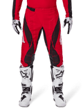 Alpinestars 2025 Techstar Dreem bukser, motocross crossbukser, klar rød og sort med vinklede mønstre og laserskårne ventilationshuller, vist med hvide motocrossstøvler og matchende handsker til off-road kørsel