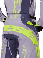 Alpinestars 2025 Techstar Dreem bukser, motocrossbukser, grå og mørkegrå med fluorescerende gule detaljer, set bagfra med tydelig Alpinestars-branding over bagstykket, vist med matchende trøje og handsker, designet til off-road racing.