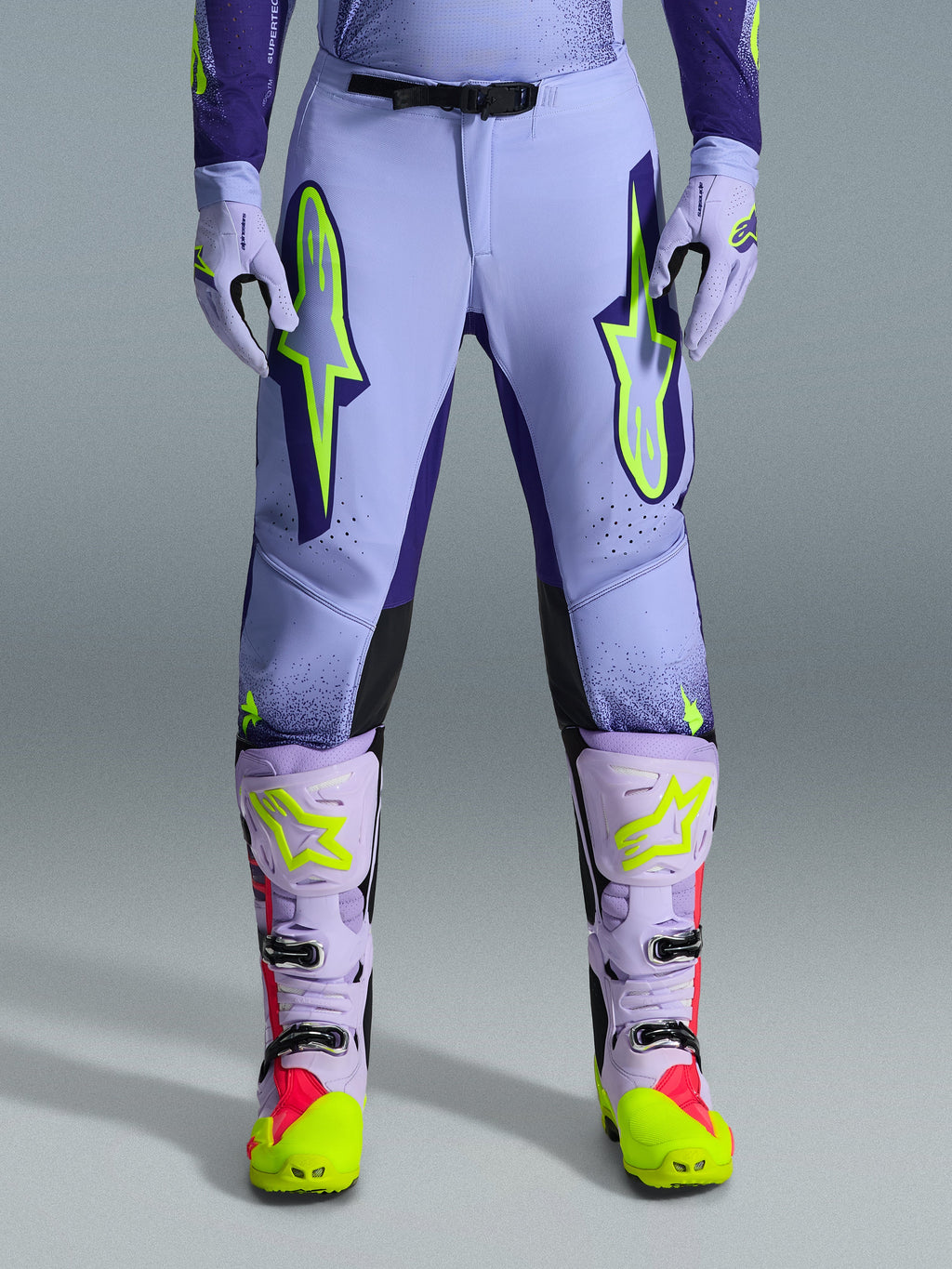 Alpinestars 2026 Supertech Scenz bukser, motocross-bukser, lilla og neon-gul, med store neon-gule logoer på lårene, vist med matchende lilla og gule motocross-støvler og -handsker, atletisk ydeevne-design til terrænkørsel
