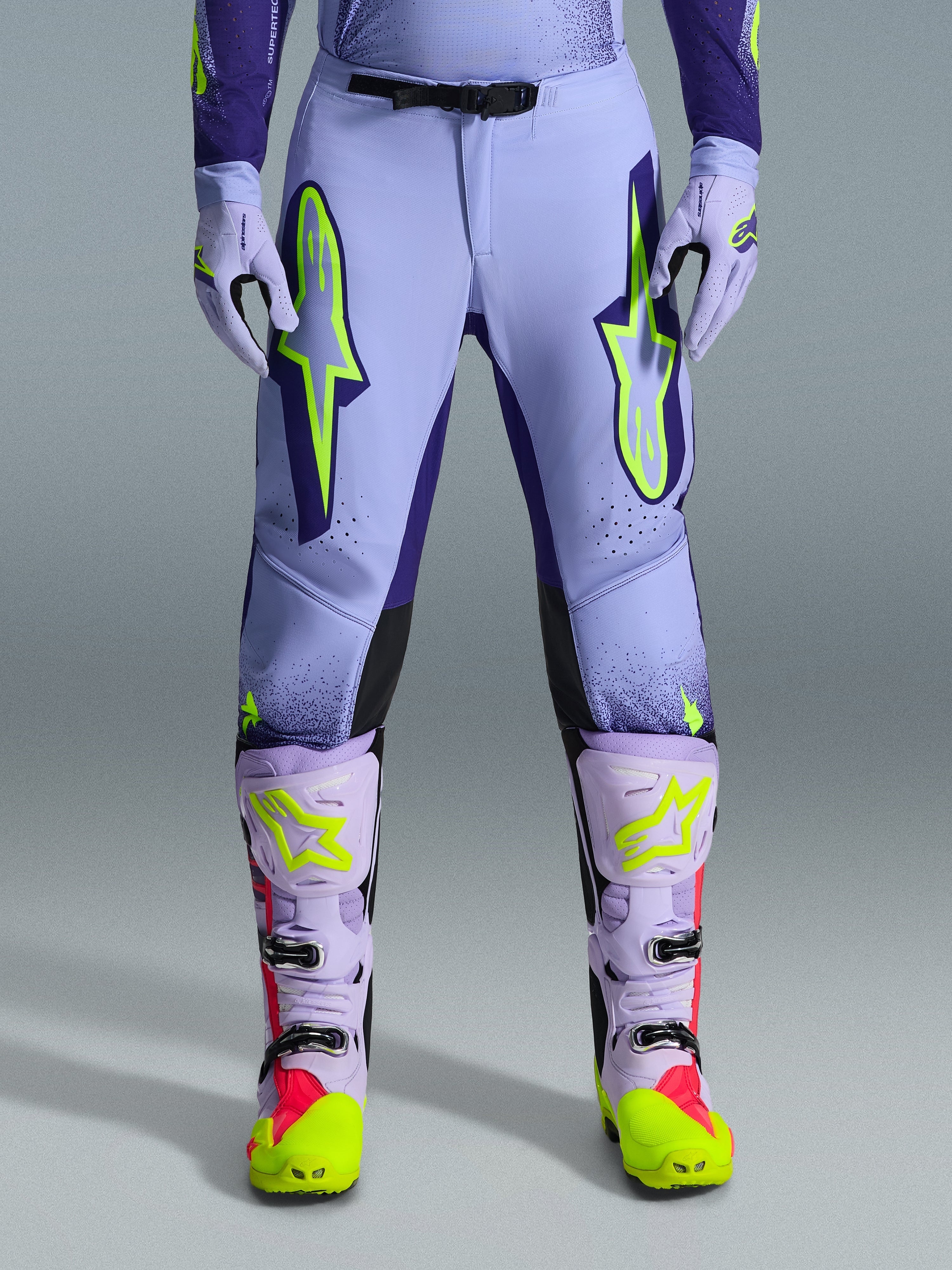 Alpinestars 2026 Supertech Scenz bukser, motocross-bukser, lilla og neon-gul, med store neon-gule logoer på lårene, vist med matchende lilla og gule motocross-støvler og -handsker, atletisk ydeevne-design til terrænkørsel