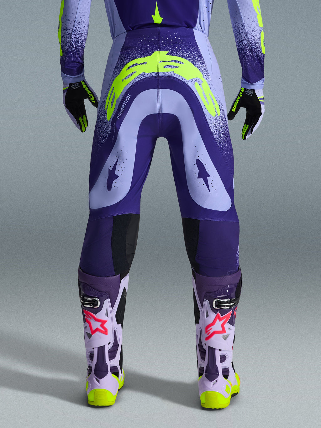 Alpinestars 2026 Supertech Scenz bukser, motocross-bukser, lilla og neon-gul, set bagfra med stort gult logo på bagdelen, båret med matchende trøje, handsker og beskyttelsesstøvler, atletisk pasform til professionel motocross-racing