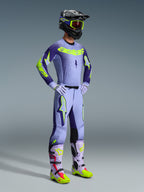 Alpinestars 2026 Supertech Scenz bukser, motocross-bukser, lilla og neongul, båret af en kører i et komplet raceroutfit med en matchende jersey med farveovergang, lilla handsker og koordinerede gule og lilla støvler, inklusiv sort hjelm og goggles.