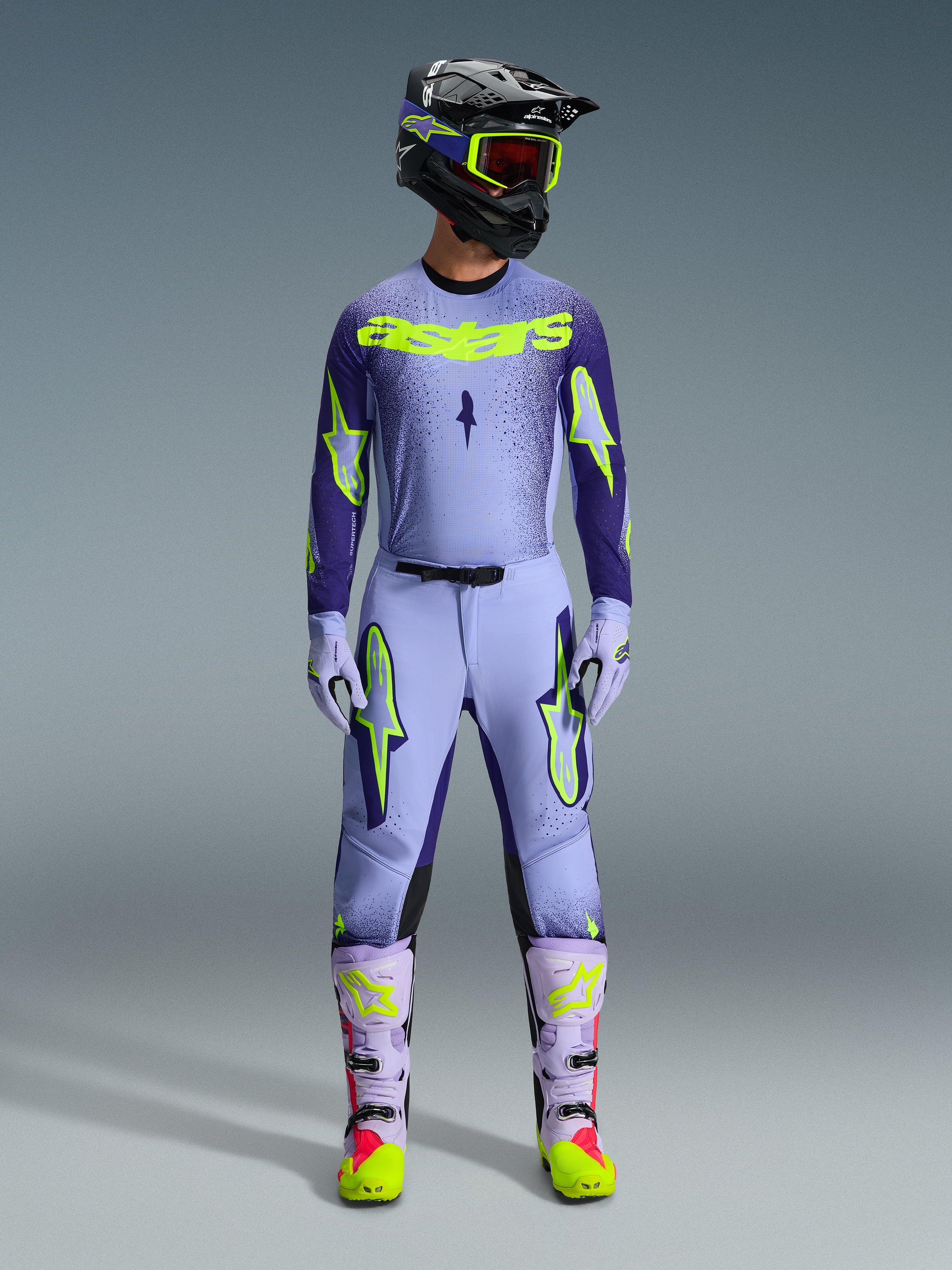 Alpinestars 2026 Supertech Scenz bukser, motocross-bukser, lilla og gul fluo, båret som et komplet racersæt med matchende lavendelfarvet trøje, handsker og støvler, markante gule fluo-logoer, atletisk pasform til professionel terrænkørsel