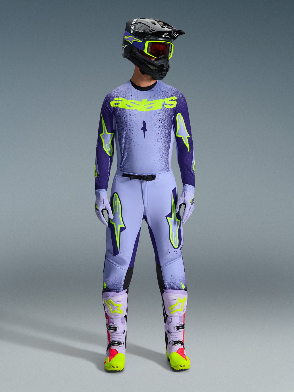 Alpinestars 2026 Supertech Scenz udstyrssæt, motocross raceroutfit, lys lilla og neongul-grøn, komplet beskyttelsesudstyr inklusive sort hjelm med lilla detaljer, jersey med markant neongul branding, matchende bukser med stjernegrafik og koordinerede støvler med pink detaljer.