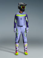 Alpinestars 2026 Supertech Scenz udstyrssæt, motocross raceroutfit, lys lilla og neongul-grøn, komplet beskyttelsesudstyr inklusive sort hjelm med lilla detaljer, jersey med markant neongul branding, matchende bukser med stjernegrafik og koordinerede støvler med pink detaljer.
