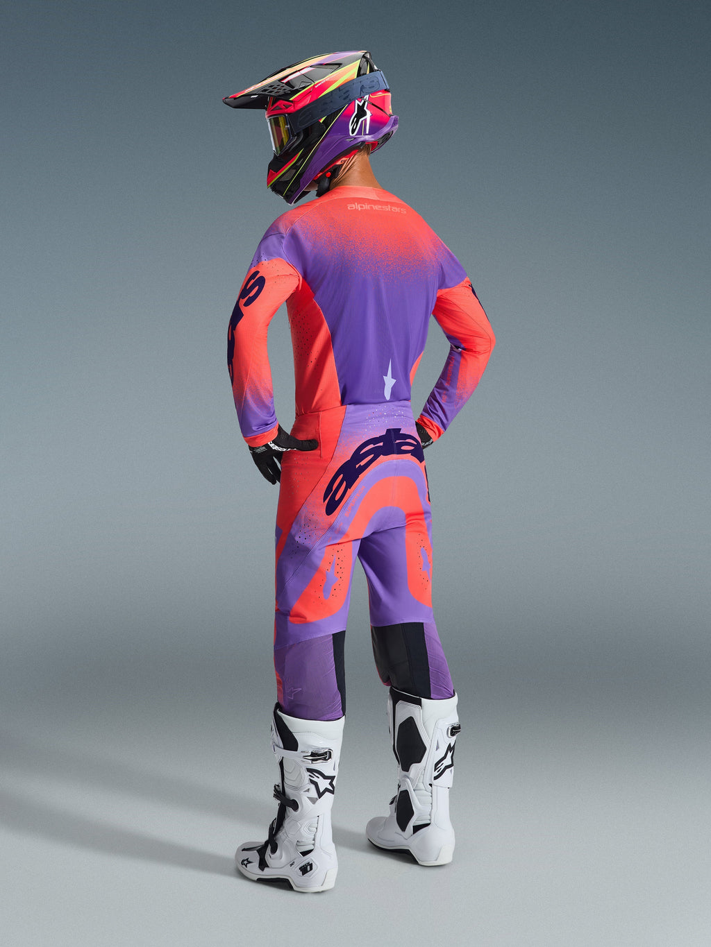 Alpinestars 2026 Supertech Scenz-bukser, motocross-bukser, Hot Coral og lilla, set bagfra med markant branding på sædet, båret af en kører med matchende trøje og hvide støvler, professionelt off-road racingudstyr
