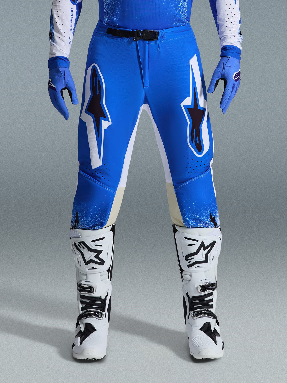 Alpinestars 2026 Supertech Scenz bukser, motocross-bukser, Ucla Blue White, vist med matchende blå handsker og hvide støvler, med store hvide og sorte grafikker på lårene, atletisk pasform til performance i terrænet