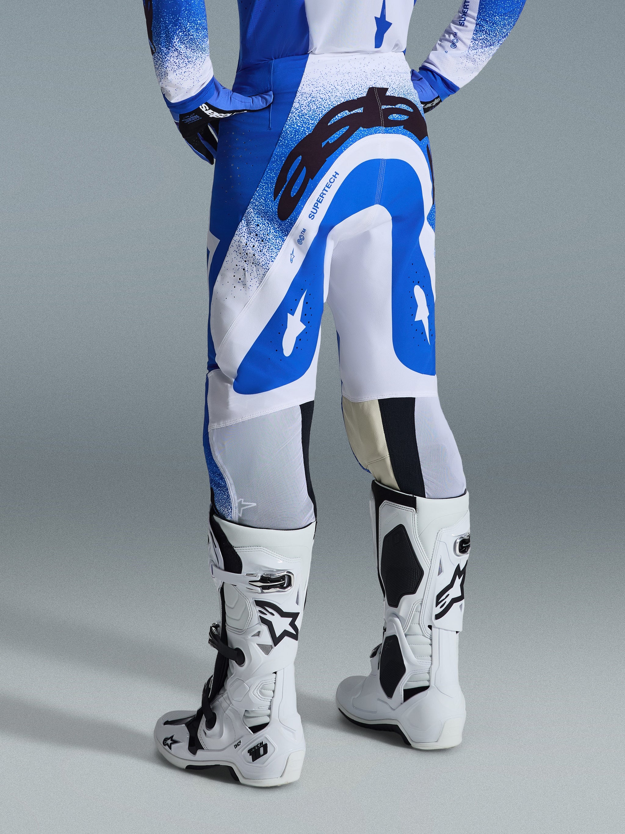 Alpinestars 2026 Supertech Scenz Pants, Motocross Pants, Ucla Blue and White, rear view showing large black Astars logo on the seat and 'SUPERTECH' branding, worn with white Tech 10 boots and a matching blue and white jersey.