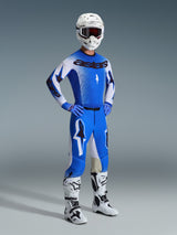 Motocross rider wearing complete racing gear, featuring the 2026 Supertech Scenz Pants in Ucla Blue and White, matching blue and white jersey with Astars logo, white helmet with red goggles, and white and black boots, coordinated outfit for professional off-road racing.