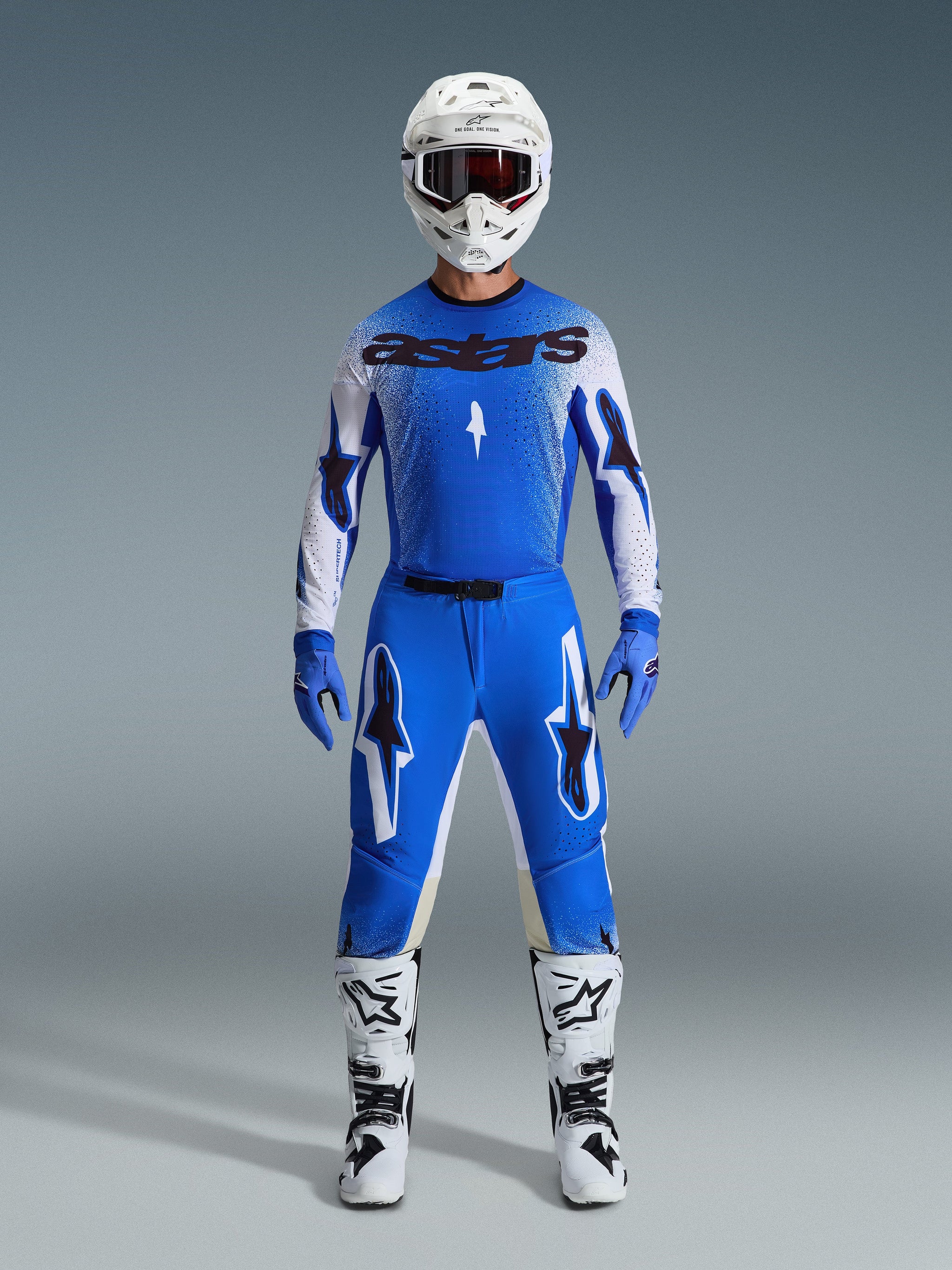 Motocross rider wearing complete racing gear, blue and white jersey with black astars branding, 2026 Supertech Scenz Pants in Ucla Blue White with bold star logos, white helmet, blue gloves, and white boots, coordinated athletic racing outfit