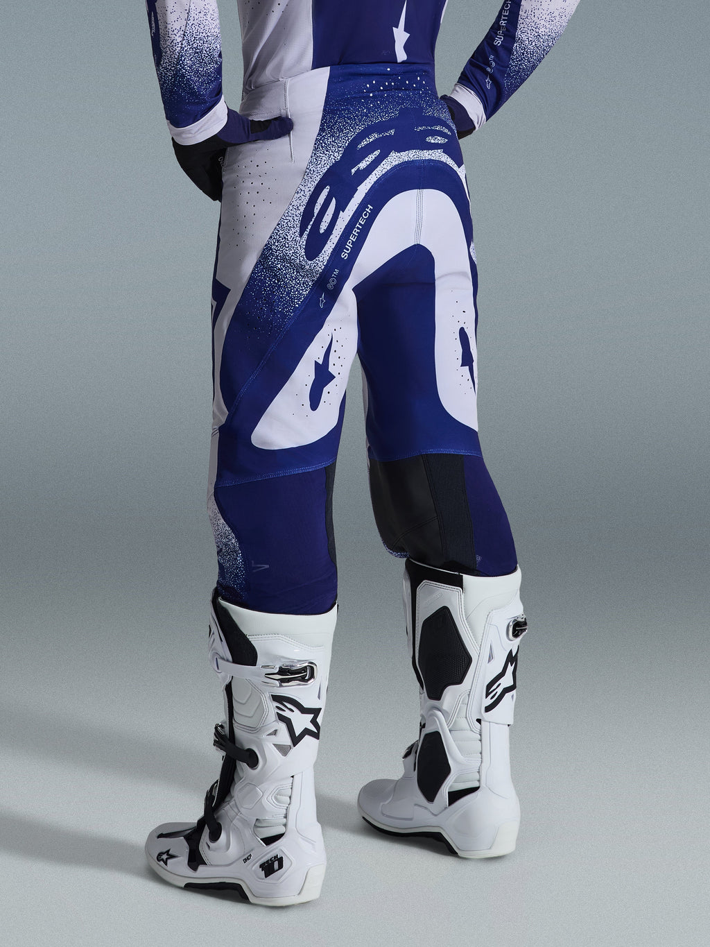 Alpinestars 2026 Supertech Scenz-bukser, motocross-bukser, lysegrå og mørkeblå, set bagfra båret med matchende trøje og hvide støvler, markant blå grafik med spættede detaljer, atletisk pasform til off-road racing.