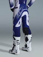 Alpinestars 2026 Supertech Scenz-bukser, motocross-bukser, lysegrå og mørkeblå, set bagfra båret med matchende trøje og hvide støvler, markant blå grafik med spættede detaljer, atletisk pasform til off-road racing.