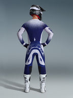 Alpinestars 2026 Supertech Scenz bukser, motocross-bukser, lysegrå og mørkeblå, set bagfra af en rytter iført et matchende udstyrssæt med spættet gradientgrafik, hvide støvler og sort hjelm, professionel atletisk pasform til terrænkørsel