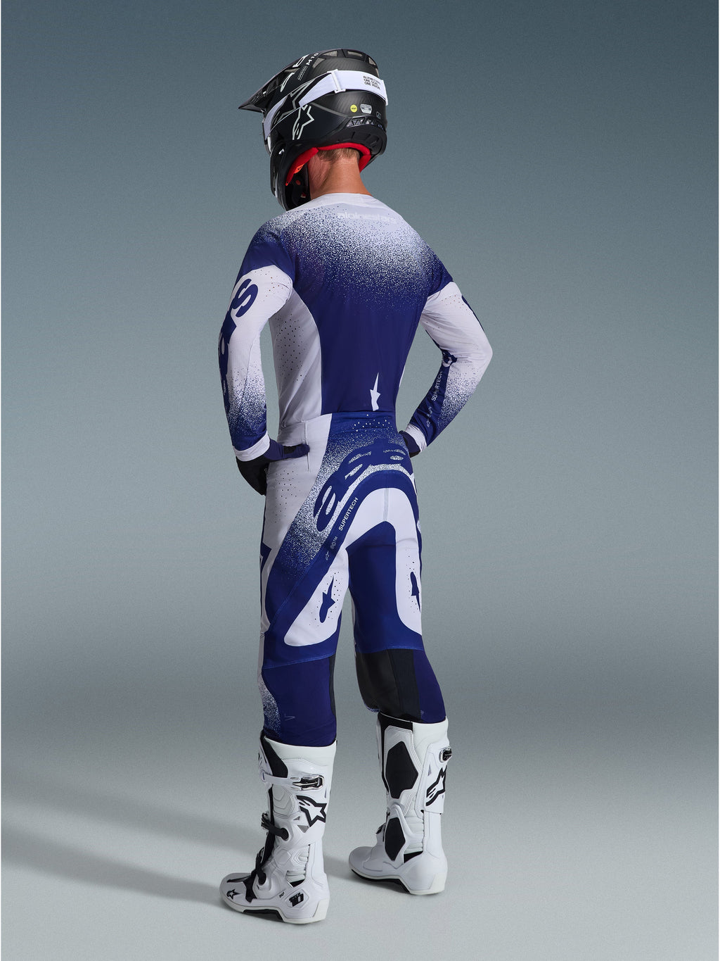 Alpinestars 2026 Supertech Scenz bukser, motocrossbukser, lysegrå og mørkeblå, set bagfra båret med matchende trøje og hvide støvler, med graduerede prik-grafikker og atletisk performance-pasform til terrænkørsel.