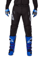 Alpinestars 2025 Racer Graphite Pants, Motocross Pants, Black and Gray, worn with blue and gray gloves and blue boots, featuring silver Astars branding on the thighs and reinforced knees, sporty design for off-road performance