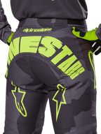 Alpinestars 2025 Racer Hollow-bukser, motocross-bukser, mørk camo og neon-gul, med et stort gult Alpinestars-logo hen over bagdelen, taktisk camouflagemønster med klare gule detaljer og slidstærk konstruktion til off-road racing.