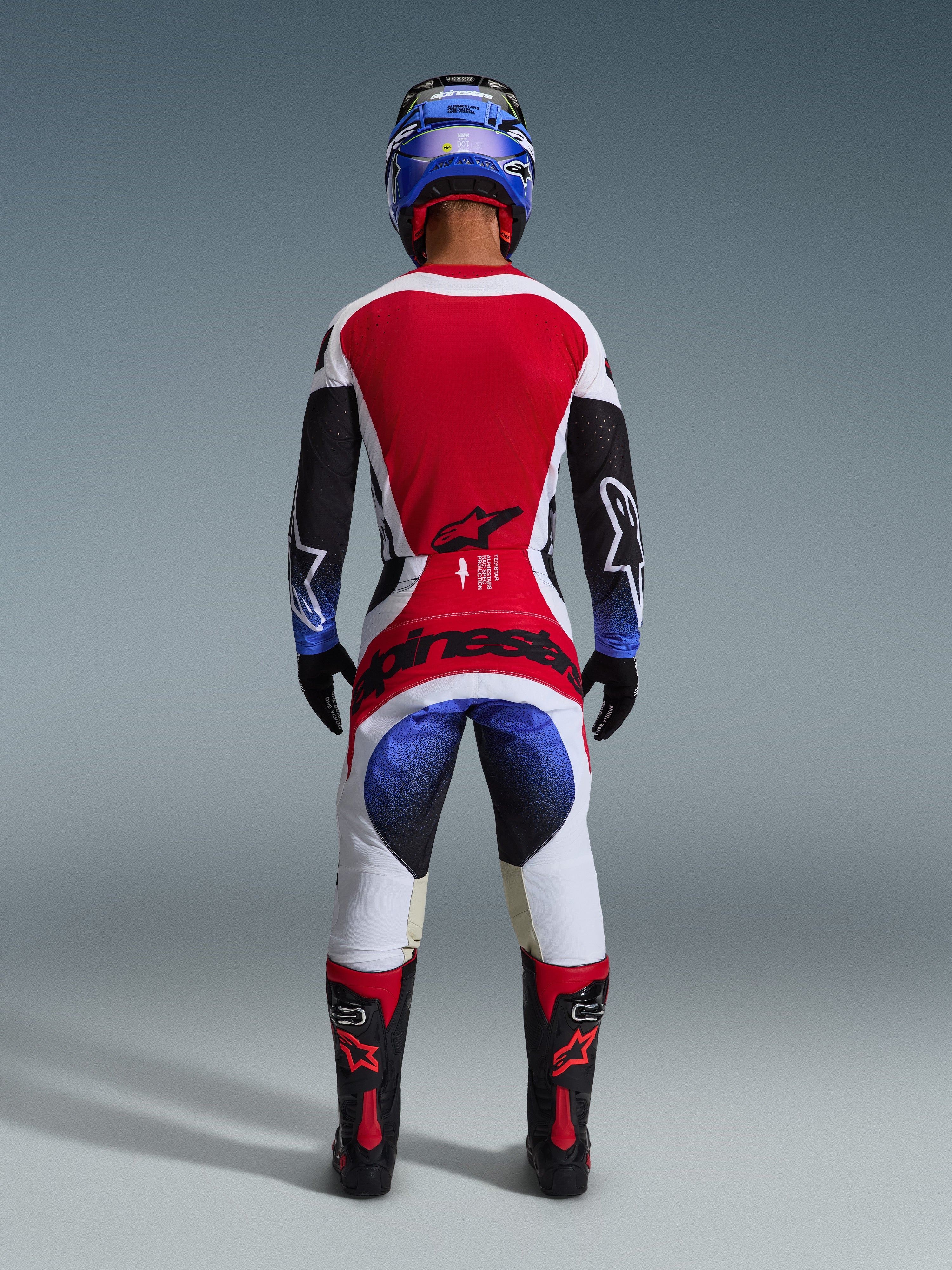 Alpinestars 2026 Techstar Knif bukser, motocross-bukser, sort hvid rød og blå, set bagfra af en rytter i komplet udstyr med matchende trøje, blå hjelm og sorte og røde støvler, tydelig Alpinestars-branding på sædet