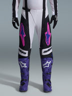 Alpinestars 2026 Techstar Knif bukser, motocross racingbukser, sort, hvid og lilla med pink og blå detaljer, båret med lilla racingstøvler og sorte handsker, med ergonomisk racingsnit og markant logografik til terrænkørsel
