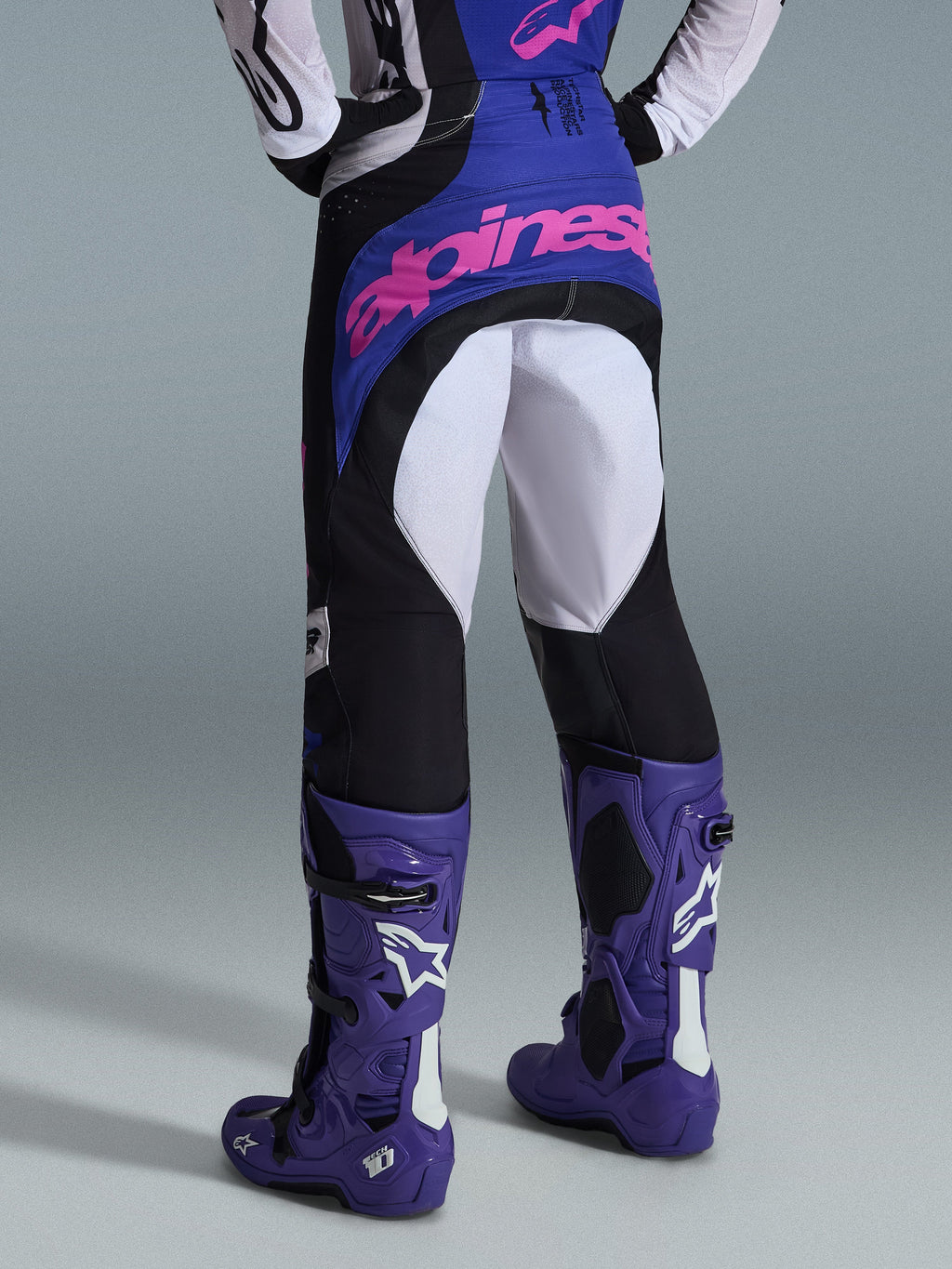 Alpinestars 2026 Techstar Knif bukser, motocross-bukser, sort, lysegrå og lilla, set bagfra med pink branding på sædet, båret med matchende trøje og lilla motocross-støvler, professionelt off-road racing-outfit