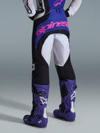 Alpinestars 2026 Techstar Knif bukser, motocross-bukser, sort, lysegrå og lilla, set bagfra med pink branding på sædet, båret med matchende trøje og lilla motocross-støvler, professionelt off-road racing-outfit