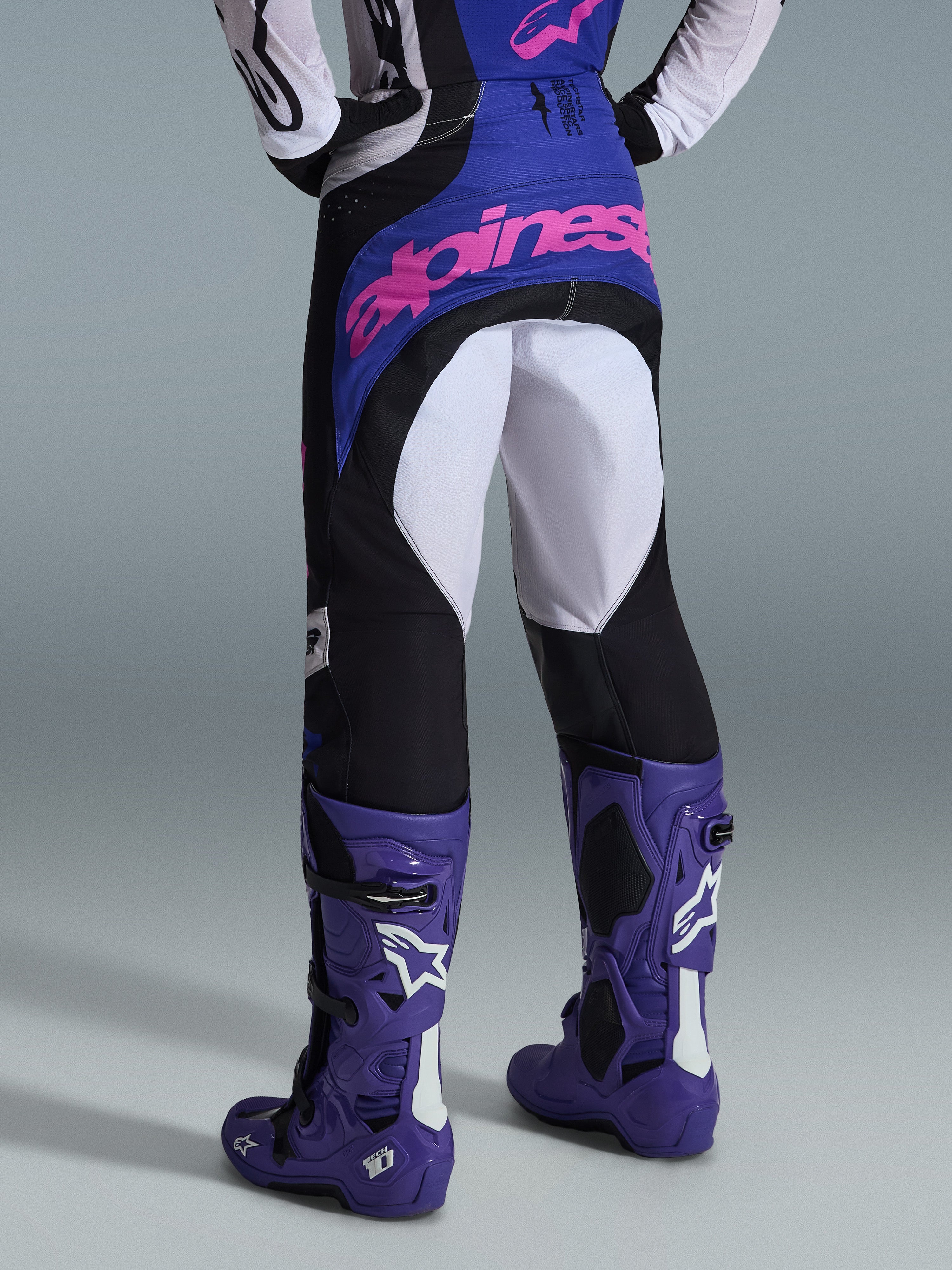 Alpinestars 2026 Techstar Knif bukser, motocross-bukser, sort, lysegrå og lilla, set bagfra med pink branding på sædet, båret med matchende trøje og lilla motocross-støvler, professionelt off-road racing-outfit