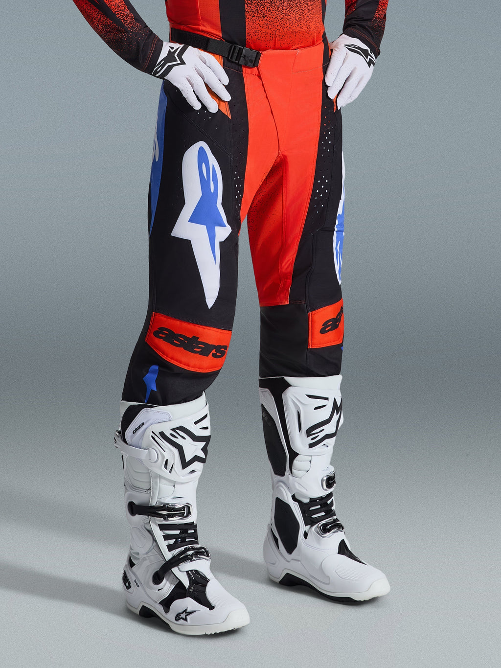 Alpinestars 2026 Techstar Knif bukser, motocross-bukser, orange, sort og UCLA-blå, båret med hvide handsker og hvide og sorte motocross-støvler, med markante logoer på lårene og orange knæpaneler med astars-branding.