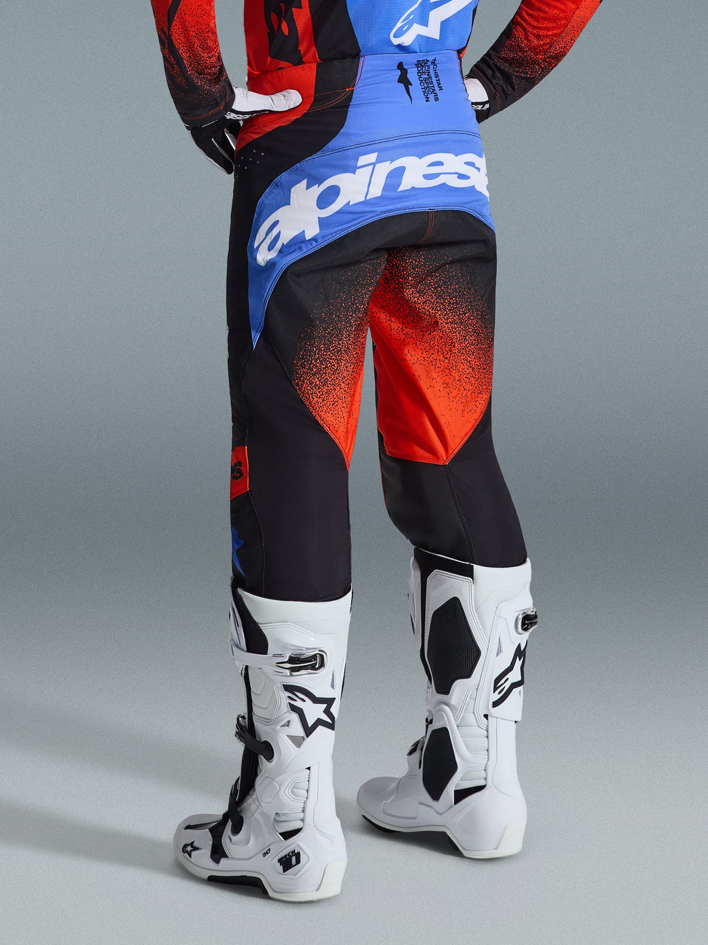 Alpinestars 2026 Techstar Knif bukser, motocrossbukser, orange, sort og UCLA-blå, set bagfra med blåt bærestykke og hvidt Alpinestars-logo, orange gradientmønster på benene, båret med matchende trøje og hvide støvler til off-road kørsel.