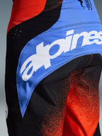 Nærbillede af Alpinestars 2026 Techstar Knif bukser, motocross-bukser, orange, sort og UCLA-blå, med stort hvidt Alpinestars-logo på et blåt sidepanel, teknisk stof med orange gradientprint, atletisk race-pasform til off-road-performance