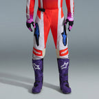Alpinestars 2026 Techstar Knif Gear Set, underkrop af motocrosskører iført røde og hvide bukser med blå detaljer, lilla racingstøvler med hvide logoer og matchende sorte og lilla handsker, professionelt udstyr til terrænkørsel