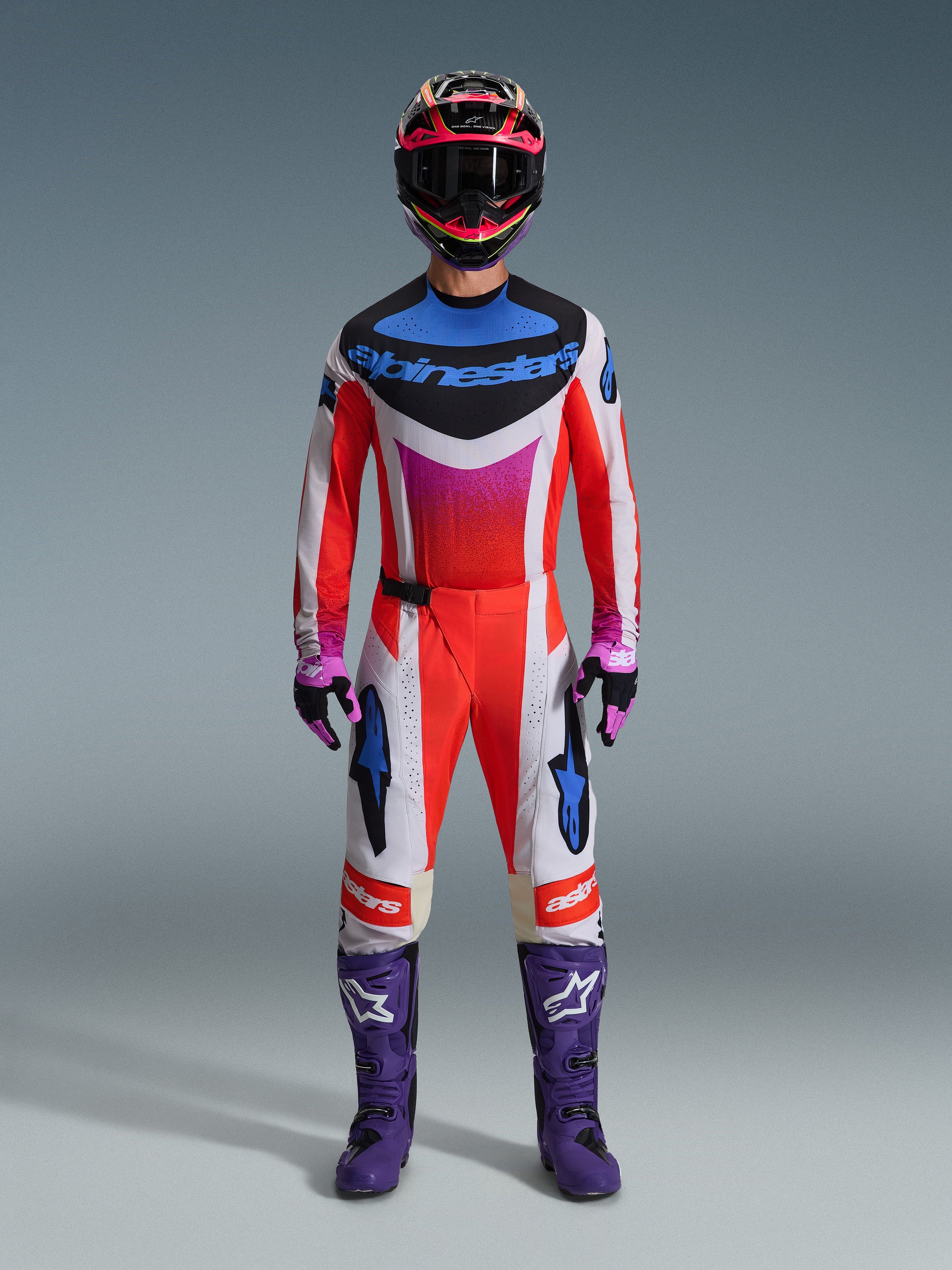 Motocrosskører iført 2026 Techstar Knif Gear Set, komplet raceroutfit i rød, hvid og sort med blå branding og pink detaljer, med lilla støvler med hvide logoer, pink og sorte handsker og en sort og pink hjelm, professionelt off-road racingudstyr
