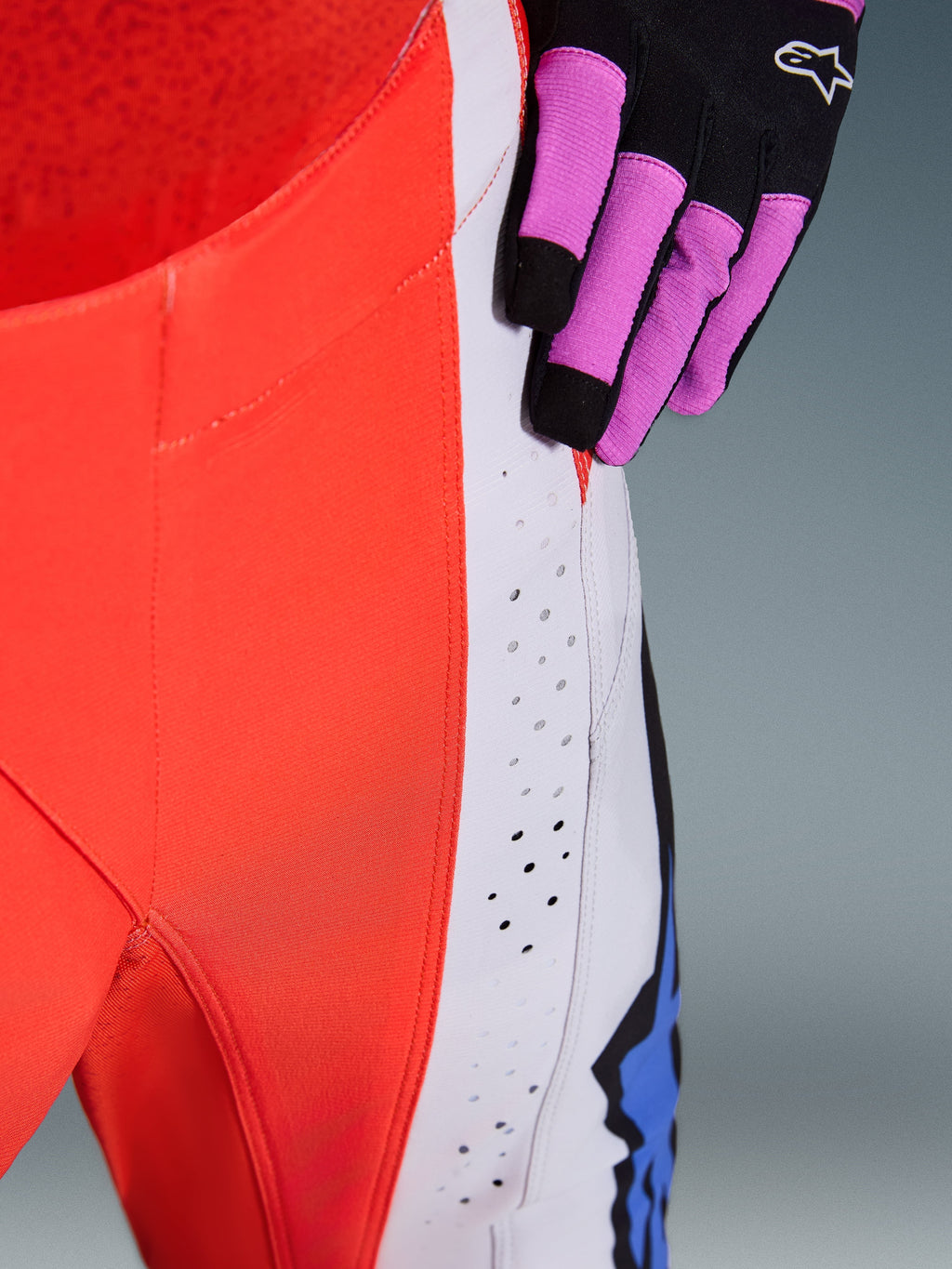 Alpinestars 2026 Techstar Knif bukser, motocross-bukser, neonorange og lysegrå med blå detaljer, nærbillede der viser laserskårne ventilationsperforeringer på låret, båret med en sort og lilla motocross-handske