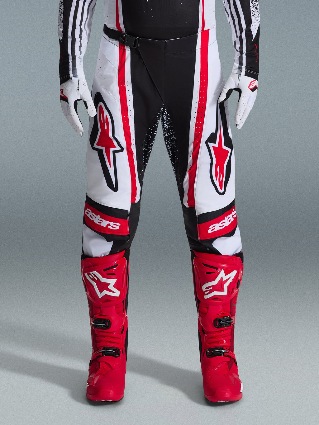 Alpinestars 2026 Techstar Nomur bukser, motocross-bukser, sort, hvid og rød, båret med matchende røde støvler og hvide handsker, med fremtrædende røde logoer på lårene og 'astars'-branding på knæene, multi-panel racingdesign til off-road ydeevne