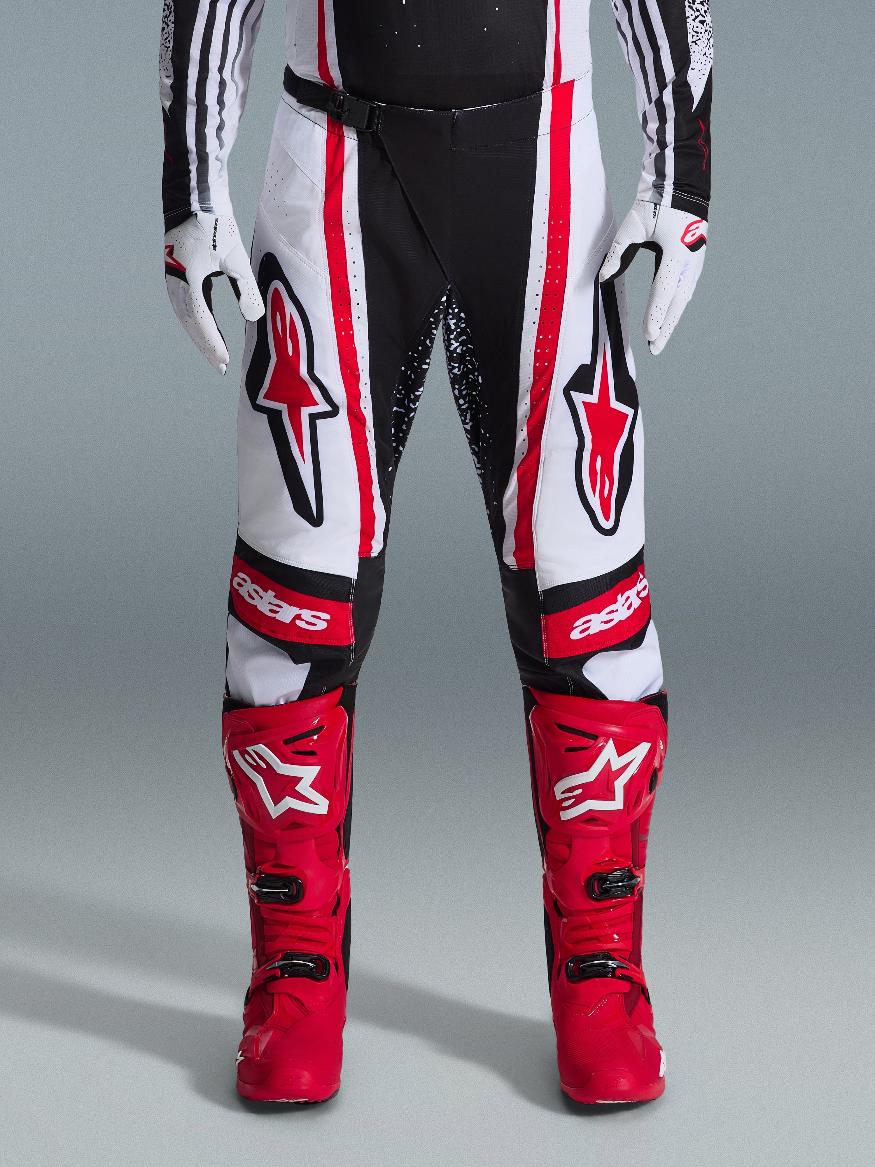 Alpinestars 2026 Techstar Nomur bukser, motocross-bukser, sort, hvid og rød, båret med matchende røde støvler og hvide handsker, med fremtrædende røde logoer på lårene og 'astars'-branding på knæene, multi-panel racingdesign til off-road ydeevne