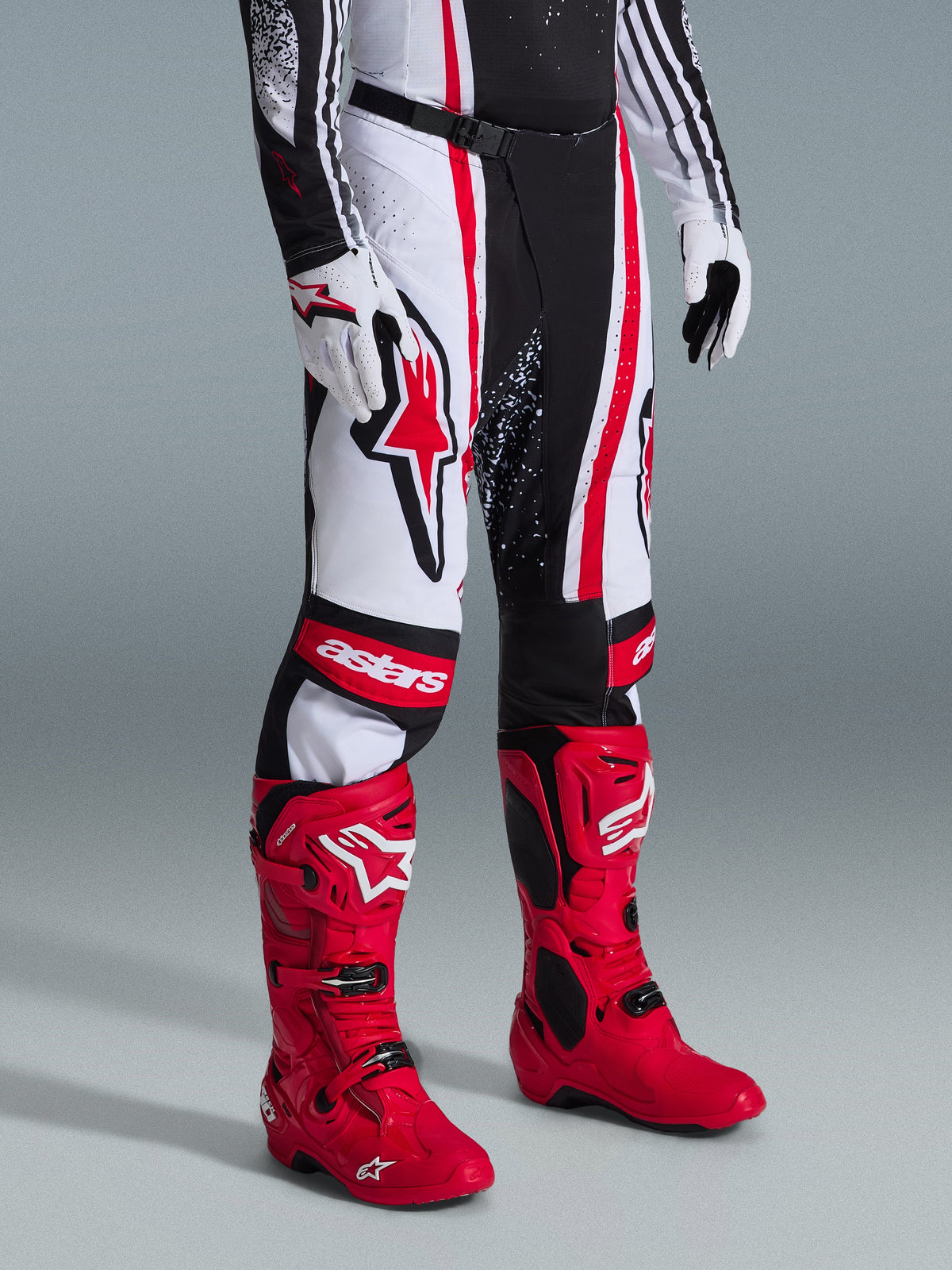 Alpinestars 2026 Techstar Nomur bukser, motocrossbukser, sort hvid rød, båret med klare røde racingstøvler og hvide handsker, med markante lodrette striber, et stort rødt stjernelogo på låret og forstærkede knæpaneler til off-road ydeevne