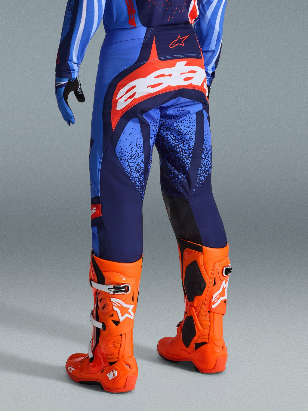 Alpinestars 2026 Techstar Nomur bukser, motocross-bukser, mørkeblå, orange og UCLA-blå, set bagfra med hvidt 'Astars'-logo på sædet, båret med klare orange motocross-støvler og matchende trøje, atletisk race-pasform til off-road-konkurrence.