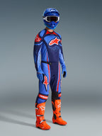 Alpinestars 2026 Techstar Nomur bukser, motocross-bukser, mørk navy, orange og UCLA blå, båret af en kører i komplet racerudstyr inklusiv en matchende trøje, blå hjelm og klare orange støvler, præstationsoptimeret til off-road racing