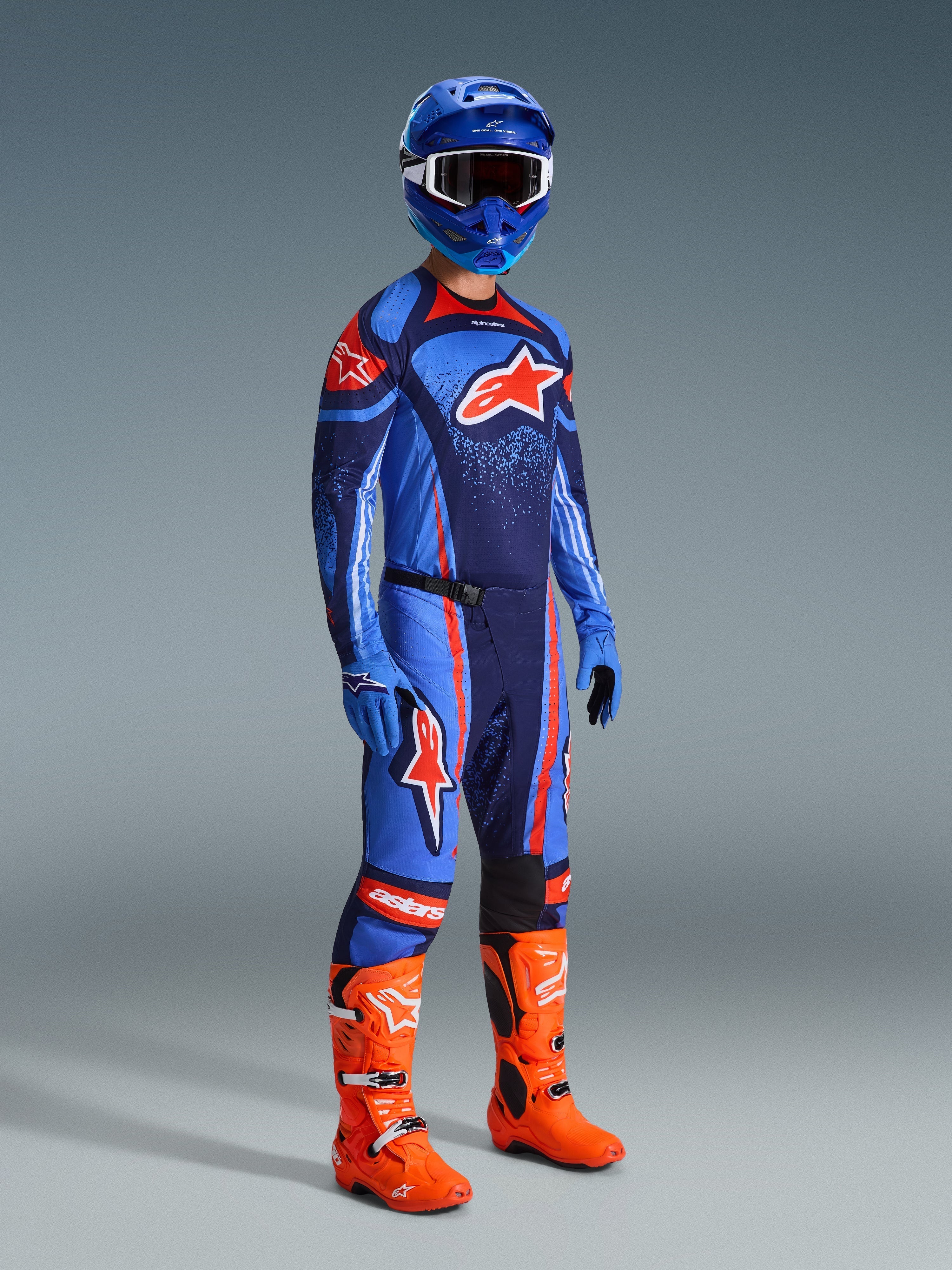 Alpinestars 2026 Techstar Nomur bukser, motocross-bukser, mørk navy, orange og UCLA blå, båret af en kører i komplet racerudstyr inklusiv en matchende trøje, blå hjelm og klare orange støvler, præstationsoptimeret til off-road racing