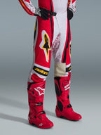 Alpinestars 2026 Techstar Nomur-bukser, motocross-bukser, rød, hvid og sort med gule detaljer, båret med matchende røde motocross-støvler og sorte handsker, med gult Alpinestars-logo og "astars"-branding på knæene, professionelt off-road racingudstyr