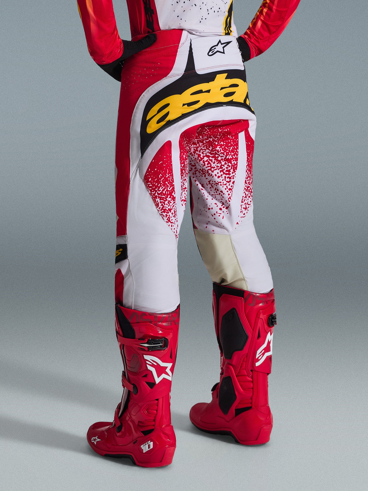 Alpinestars 2026 Techstar Nomur bukser, motocross-bukser set bagfra, rød og hvid med et markant gult logo bagpå, kombineret med knaldrøde Tech 10-motocrossstøvler, studieoptagelse på en grå baggrund
