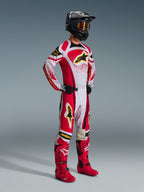 Alpinestars 2026 Techstar Nomur bukser, motocross-bukser, rød og hvid med sorte og gule detaljer, båret af en kører med en matchende racingtrøje, klare røde støvler og en sort hjelm med guldbriller, komplet professionelt off-road konkurrenceudstyr