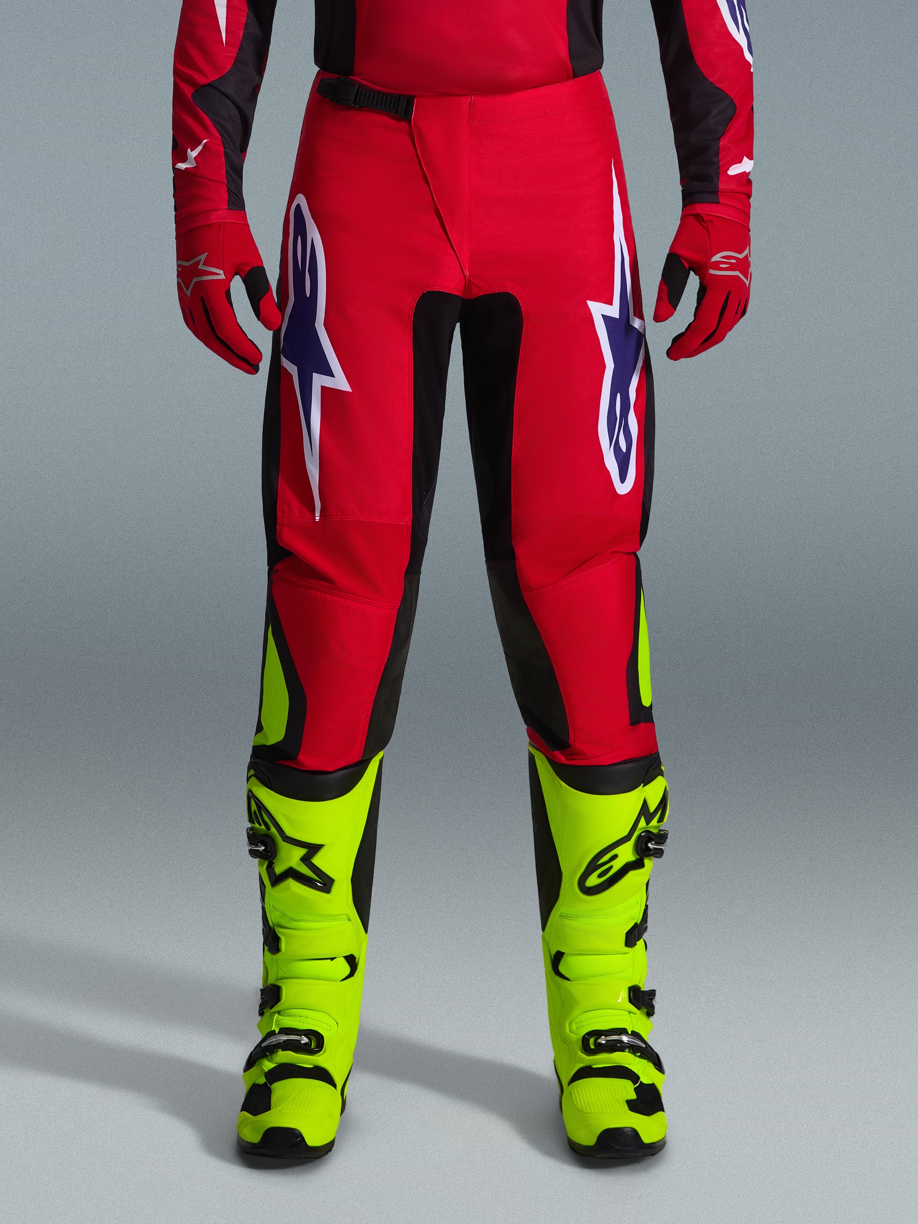 Alpinestars 2026 Fluid Grid bukser, motocross-bukser, rød med sorte paneler og neongule detaljer, med store hvide og lilla stjernelogoer på lårene, båret med røde handsker og neongule støvler, slidstærk konstruktion til off-road kørsel