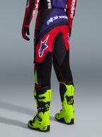 Alpinestars 2026 Fluid Grid bukser, motocrossbukser, rød, sort og lilla, set bagfra med stort hvidt logo, båret med neongule racingstøvler og matchende trøje, holdbart sport-fit design til off-road-kørsel
