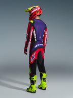 Alpinestars 2026 Fluid Grid bukser, motocrossbukser, rød, sort og lilla, set bagfra på en kører med matchende trøje og fluo-gule støvler, markant branding og ergonomisk design til off-road ydeevne.