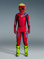 Motocross-kører iført komplet racerudstyr, Alpinestars 2026 Fluid Grid bukser i rød, sort og lilla, matchende rød og sort trøje med Alpinestars-logo, rød hjelm med fluorescerende gule detaljer, fluorescerende gule støvler og røde handsker, komplet udstyrssæt til off-road motocross-løb