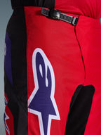 Alpinestars 2026 Fluid Grid bukser, motocrossbukser, rød, sort og lilla, tætbillede af talje- og hofteområdet med en sort skraldelukning og et stort lilla Alpinestars stjernelogo med hvidt omrids, slidstærkt tekstureret materiale til off-road racing.