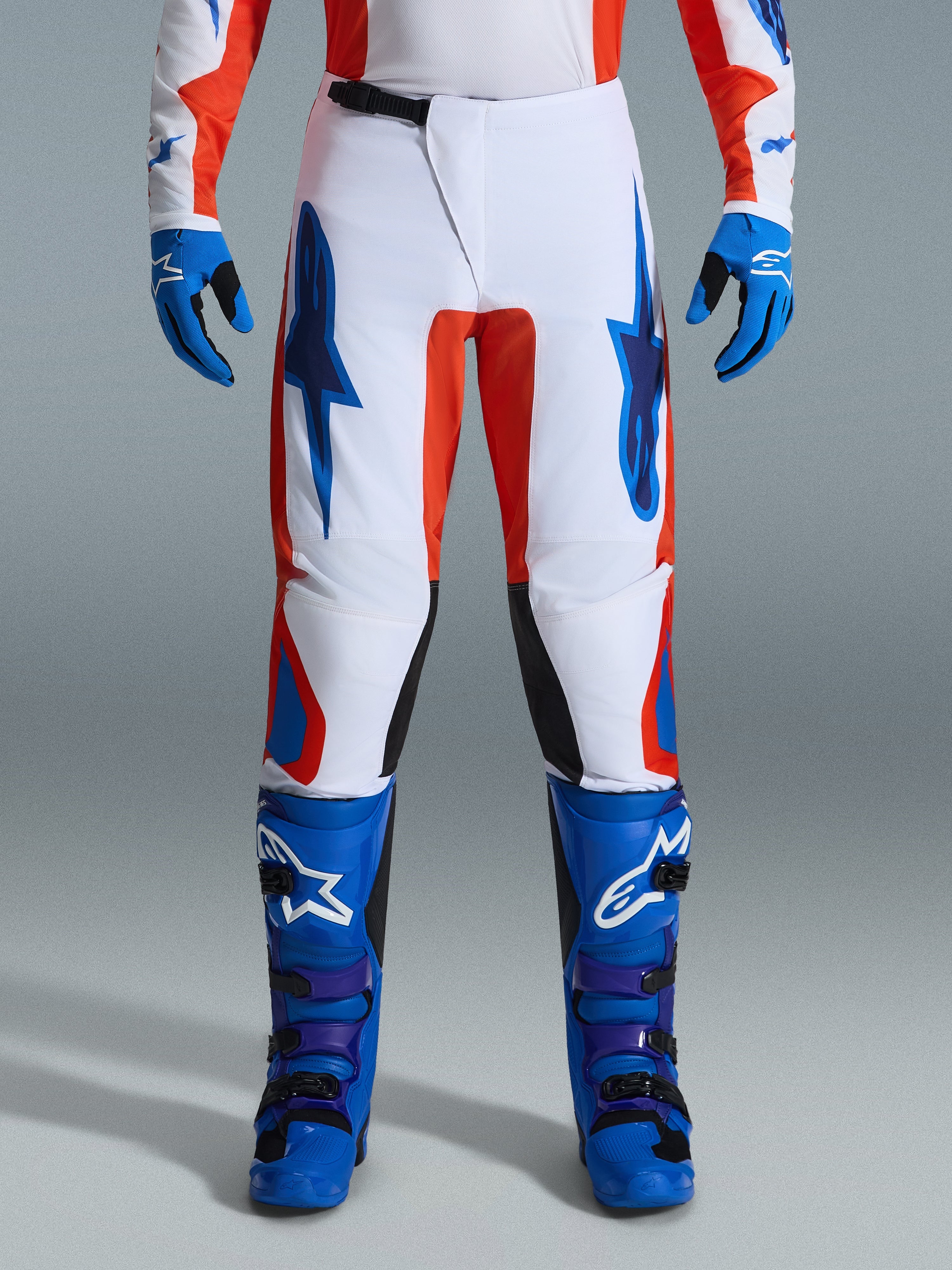 Alpinestars 2026 Fluid Grid bukser, motocrossbukser, orange og UCLA-blå, båret med matchende blå støvler og handsker, med hvidt chassis, markante blå logoer og orange detaljer, ergonomisk design til off-road ydeevne