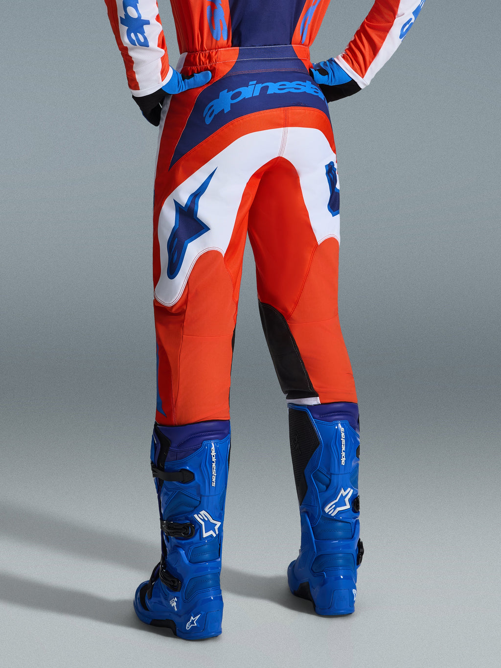 Alpinestars 2026 Fluid Grid bukser, motocross-bukser, orange og UCLA-blå med hvide paneler, set bagfra med tydeligt blåt logo på sædet og stjernelogo, kombineret med matchende blå motocross-støvler, professionelt udstyr til off-road kørsel