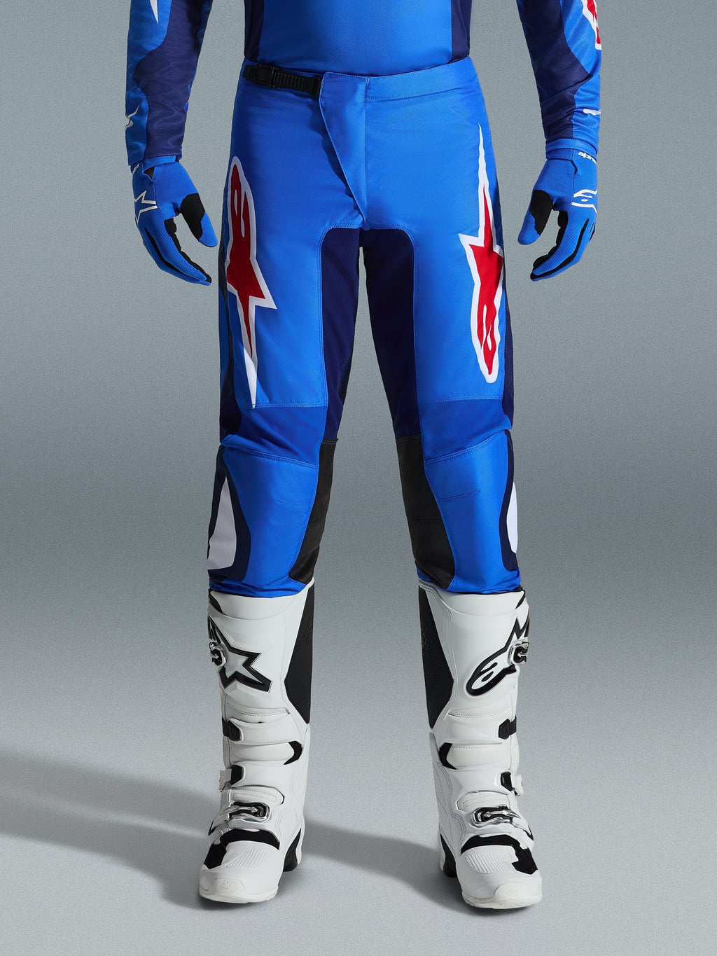 Alpinestars 2026 Fluid Grid bukser, motocross-bukser, blå og rød, med markante røde og hvide stjernelogoer på lårene, båret med matchende blå handsker og hvide off-road-støvler, atletisk pasform med holdbare paneler til racing